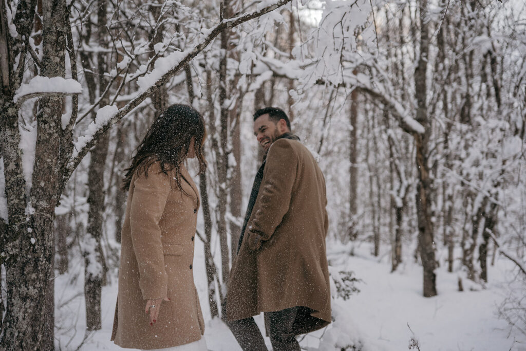 Couple walking in snowy forest, smiling warmly.