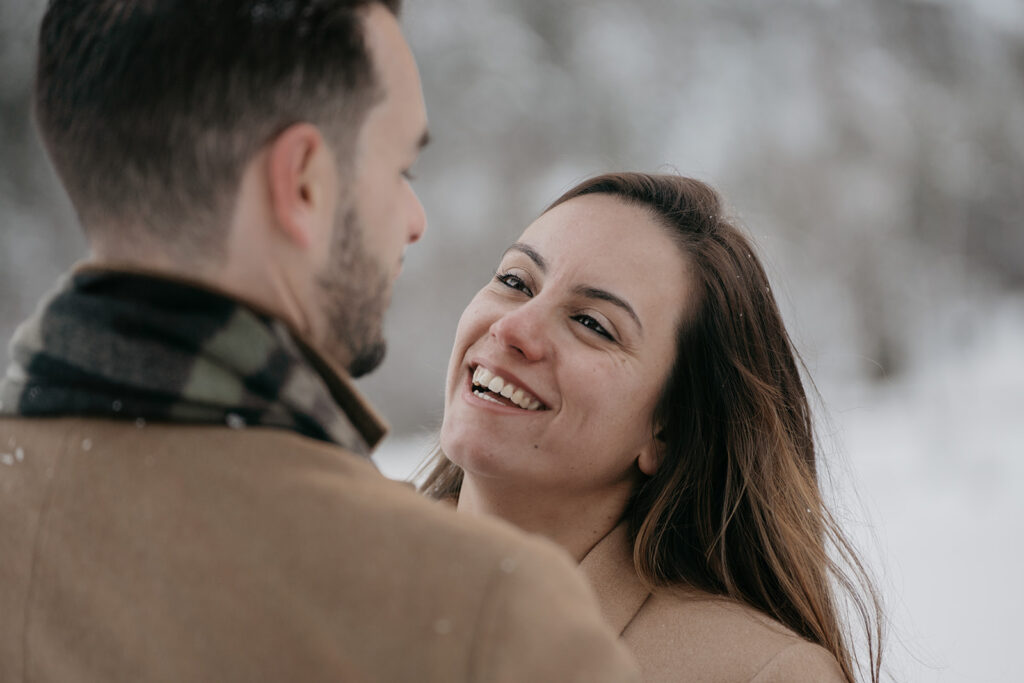 Couple smiling at each other in snowy setting.