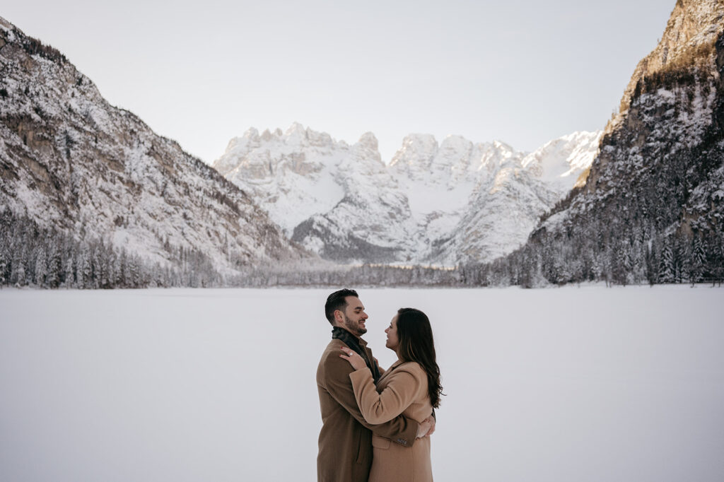 Couple embraces in snowy mountain landscape.