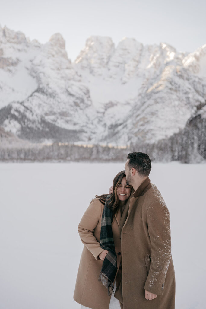 Couple embraces in snowy mountain landscape.