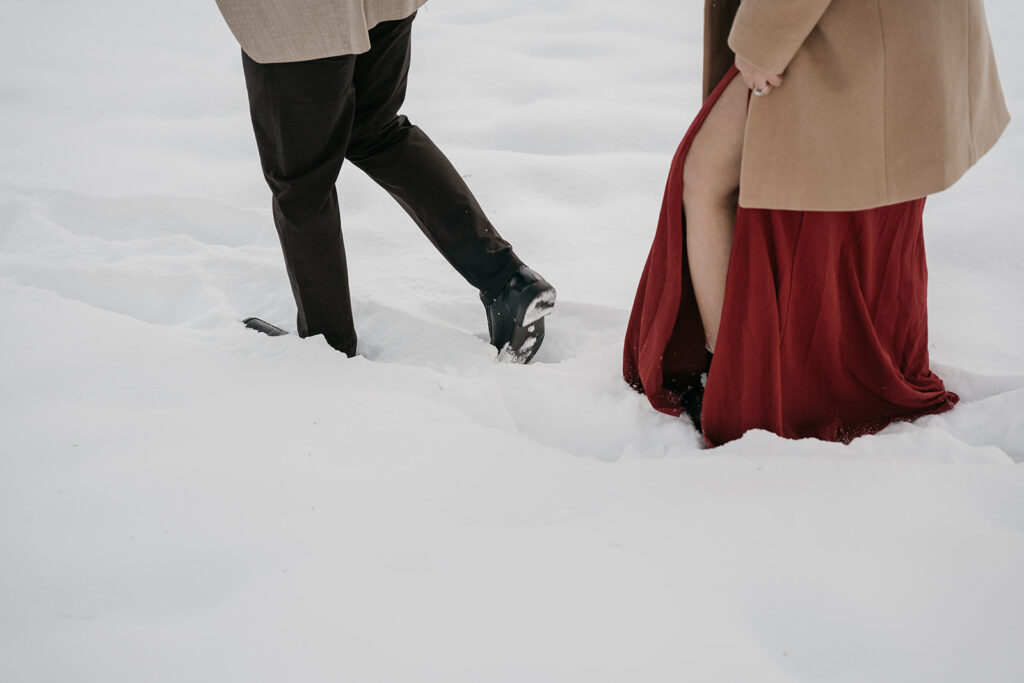 Couple walking through snow in winter clothing.