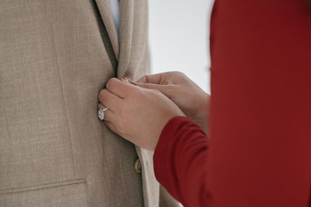 Person adjusts beige suit jacket button.