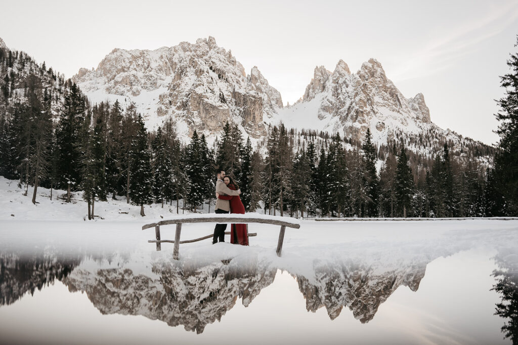 Couple embracing on snowy bridge with mountains.