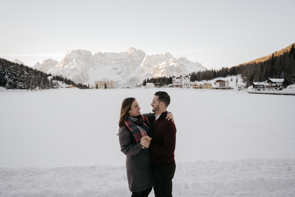 Couple embraces in snowy mountain landscape.