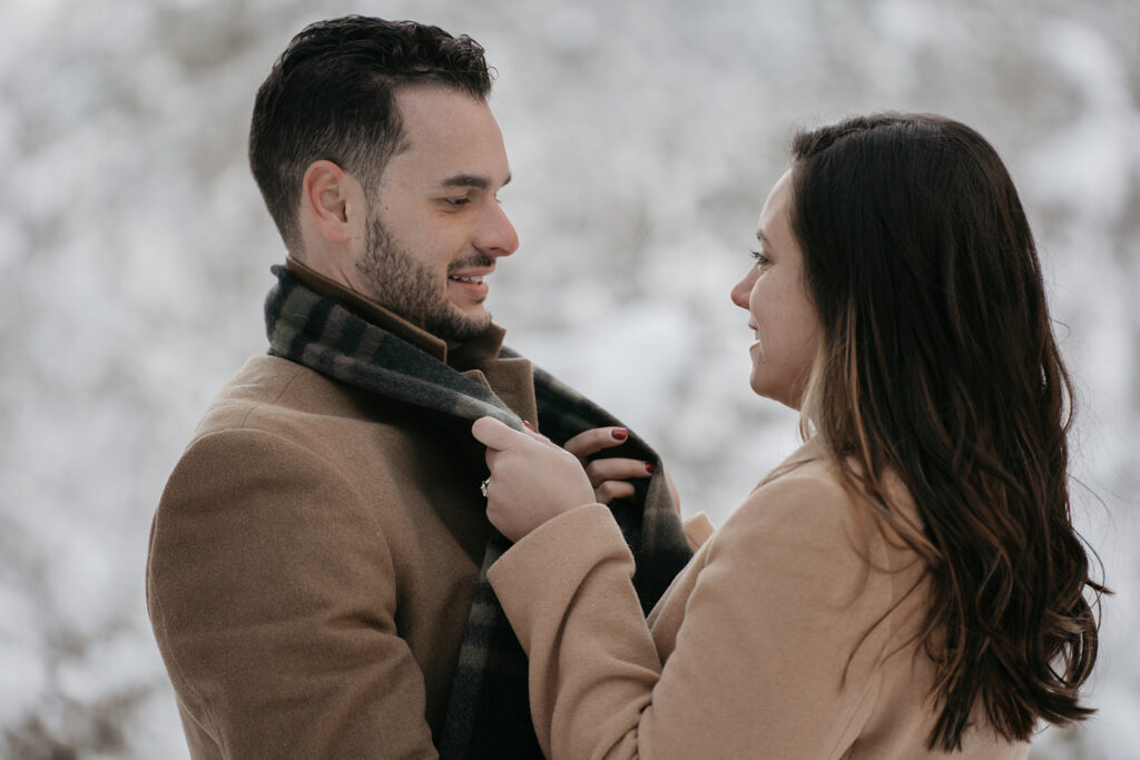 Couple embracing in winter coats against snowy backdrop.