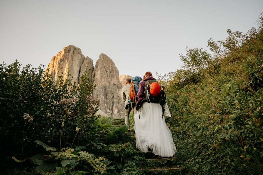 Couple hiking toward mountain, wearing backpacks and helmet.