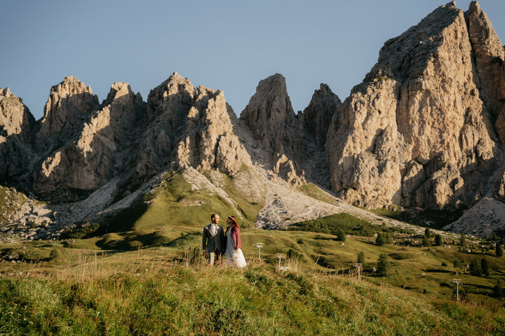 Couple standing in meadow by rocky mountains.