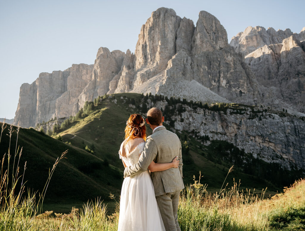 Couple embraces, gazing at mountain landscape.