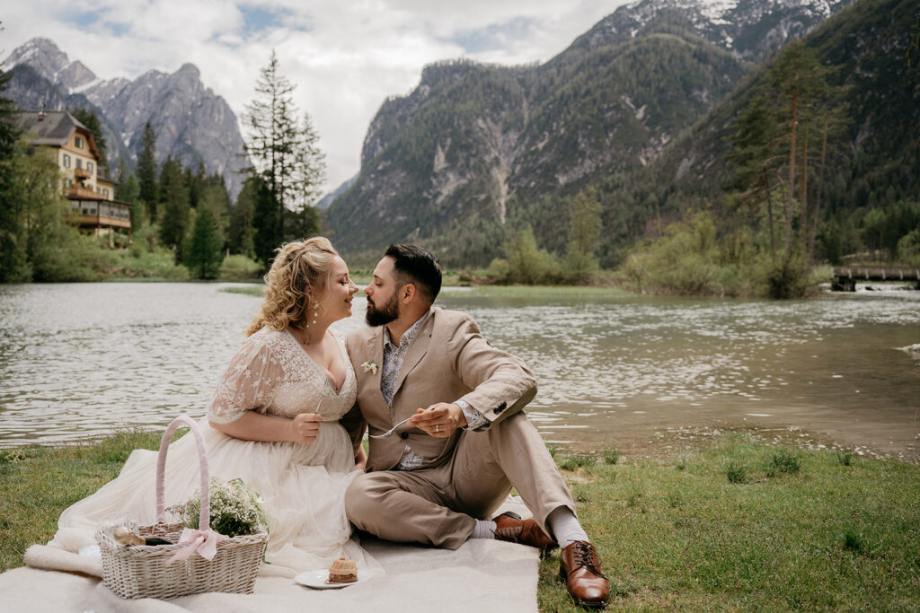 Couple picnic by lake, mountains in background.