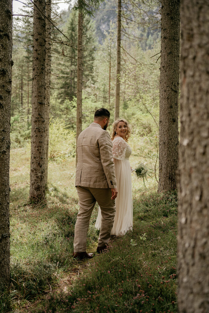 Couple walks through forest in wedding attire.