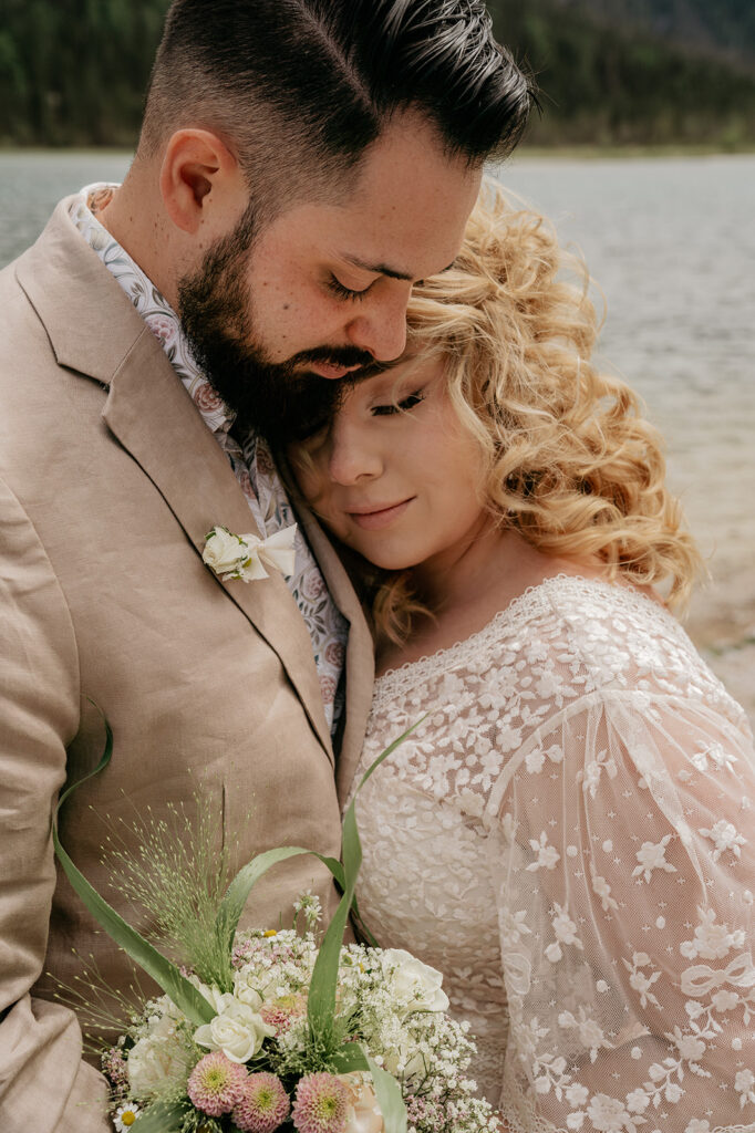 Bride and groom embracing by the water.