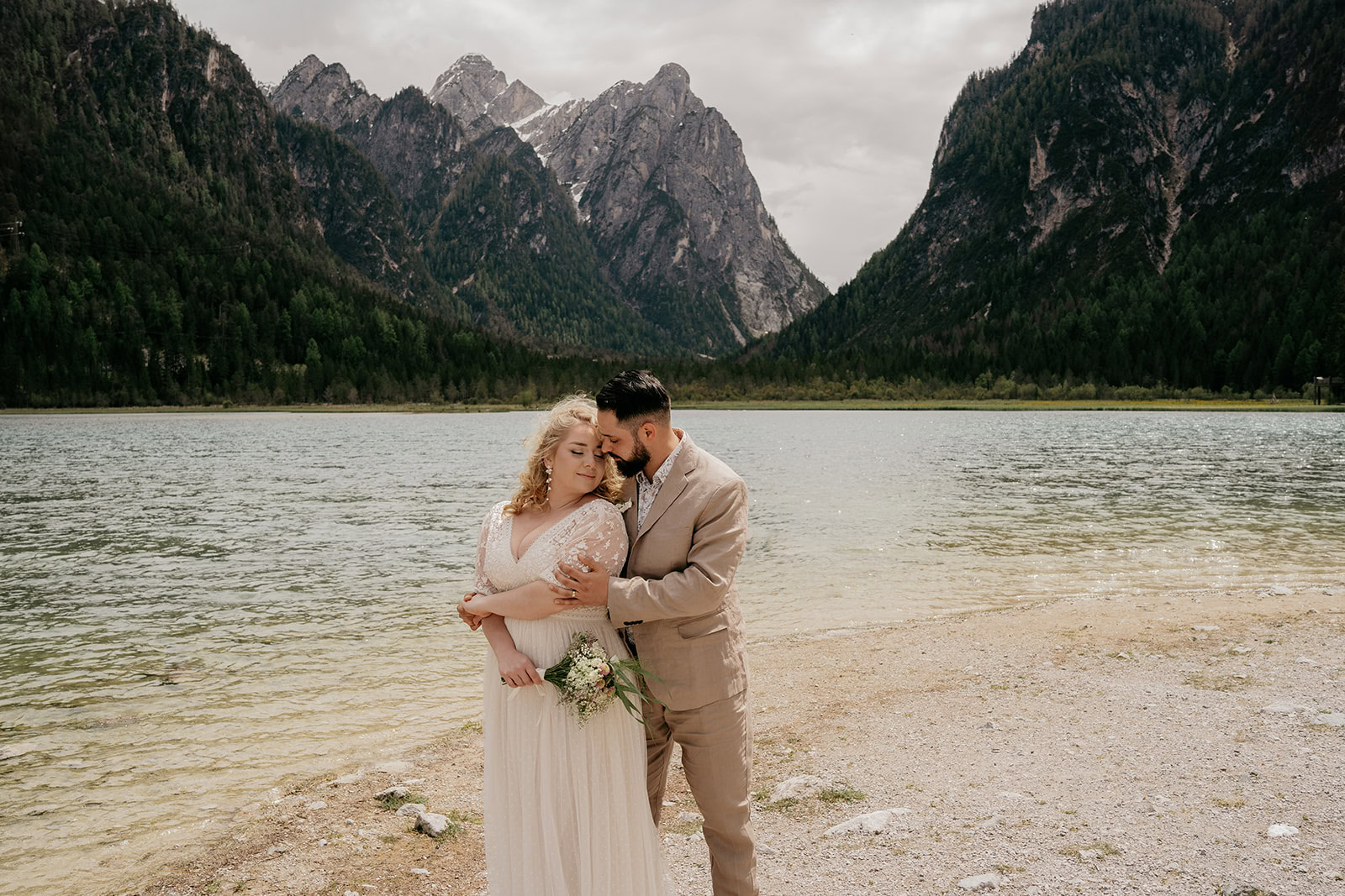 Couple embraces by mountain lake scenery.