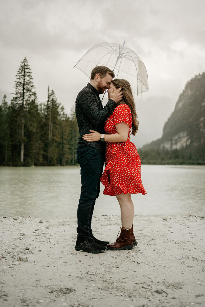 Couple embraces under umbrella by a lake.