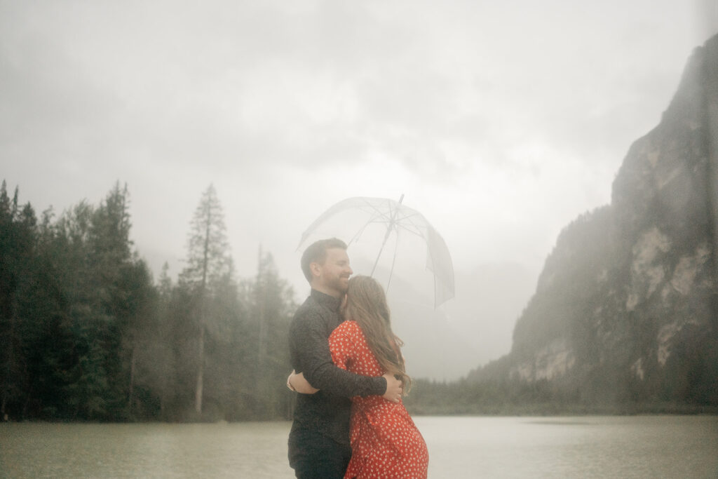 Couple hugging under umbrella by misty lake.