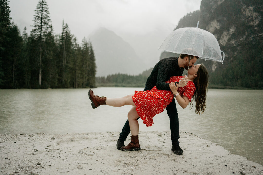 Couple kissing under umbrella by a lake.