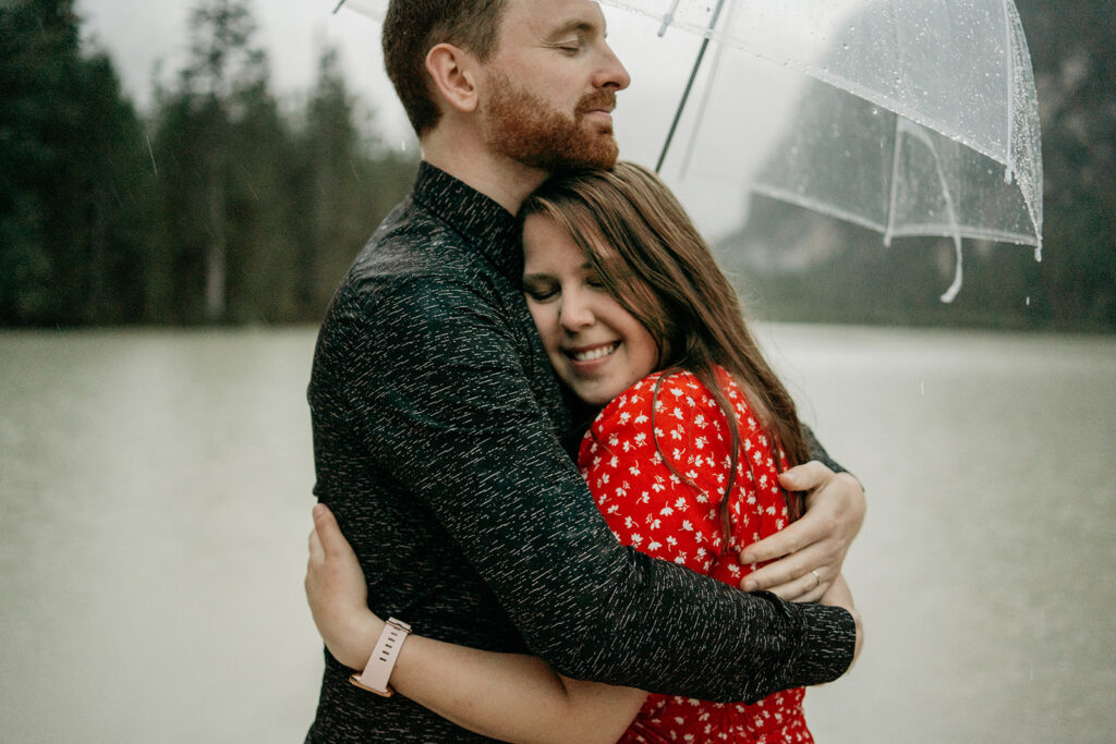 Couple hugs under umbrella by lake.