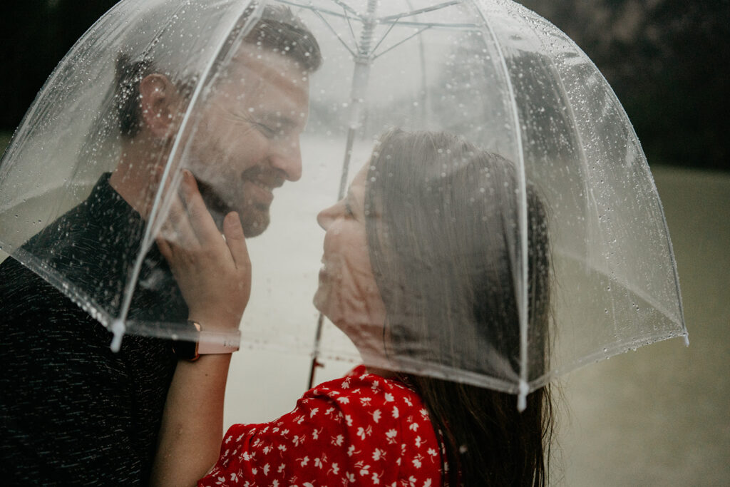 Couple under umbrella, smiling in the rain.