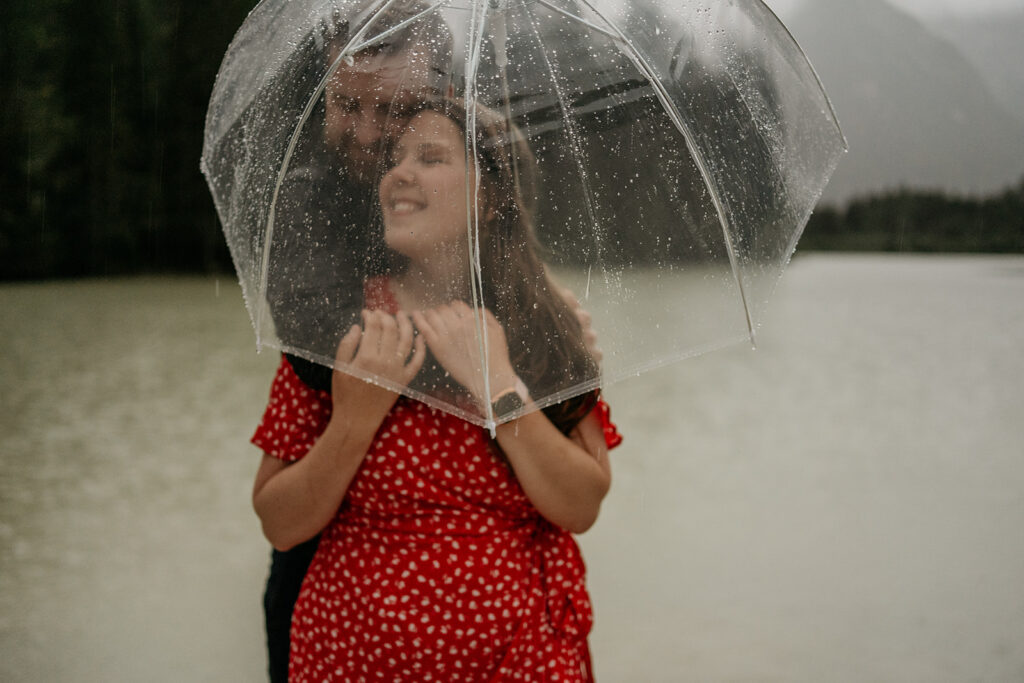 Couple under umbrella in rainy lake setting.