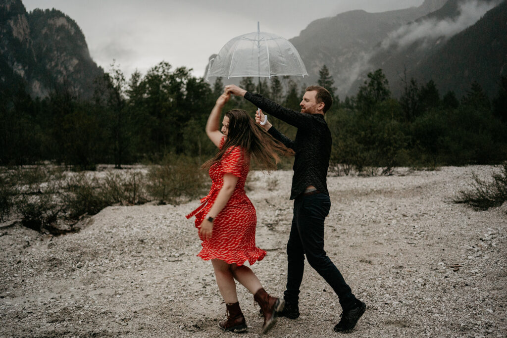 Couple dancing with umbrella in scenic mountains.