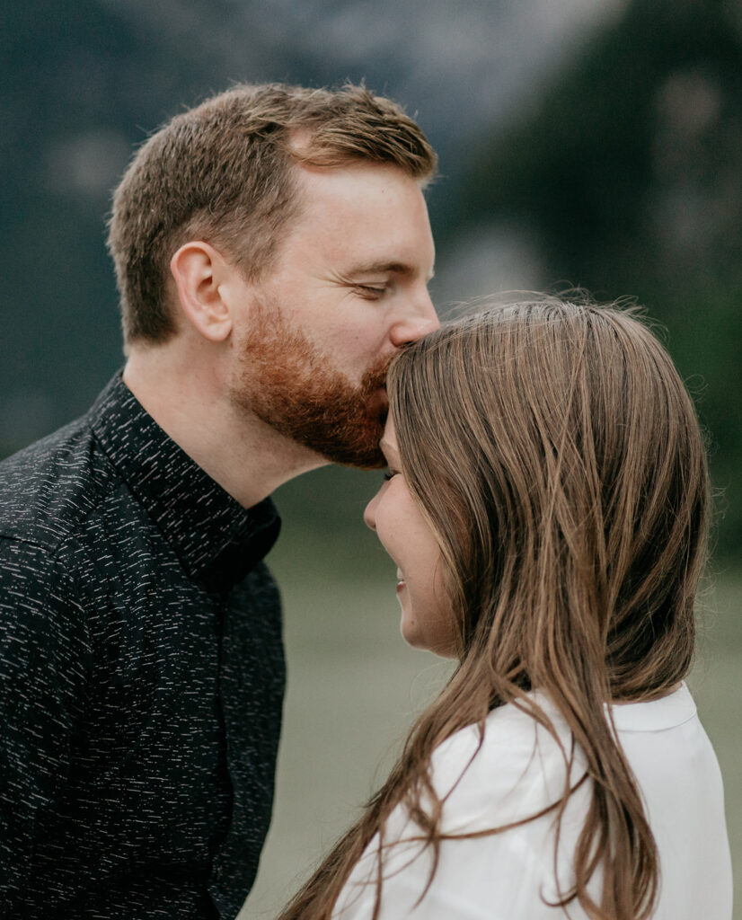 Man kisses woman's forehead, nature background.