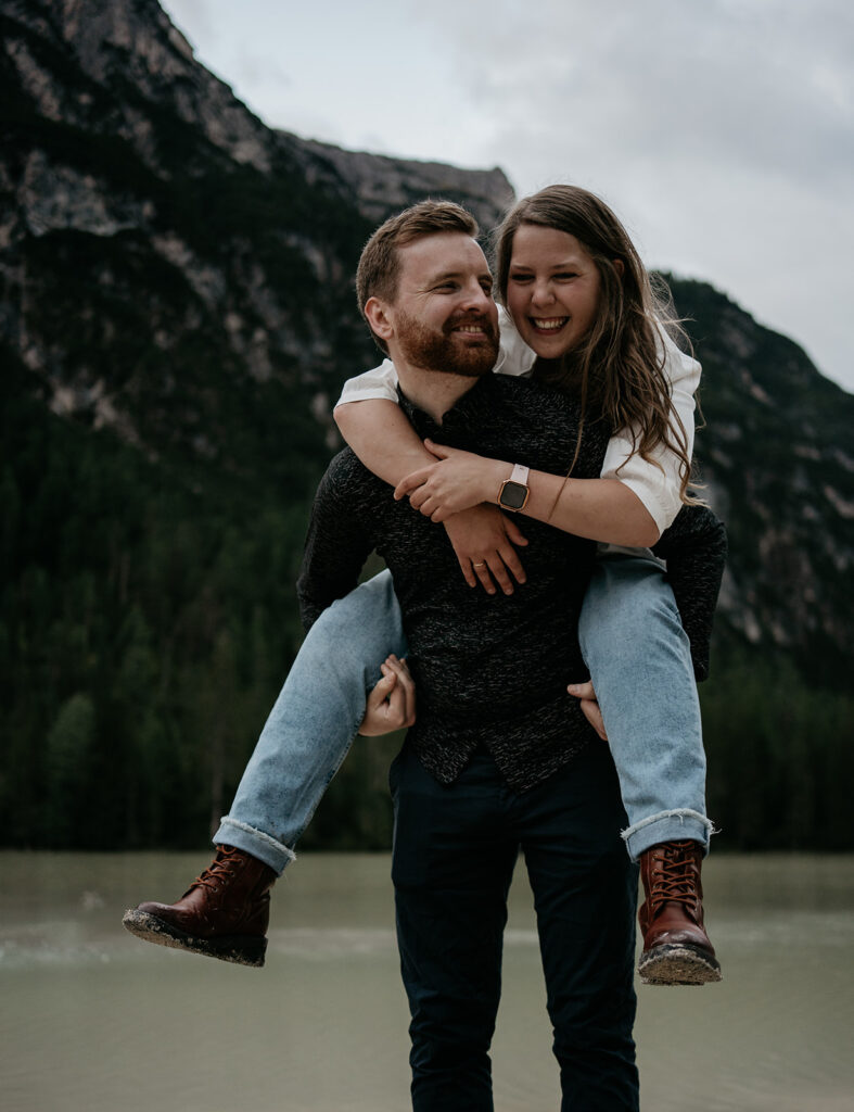 Smiling couple piggyback near scenic mountain lake.