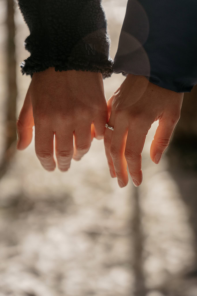 Couple holding hands with engagement ring visible.