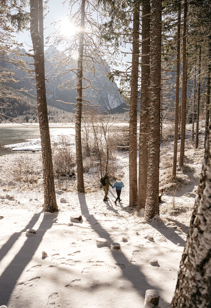 Couple walks through snow-covered forest trail.