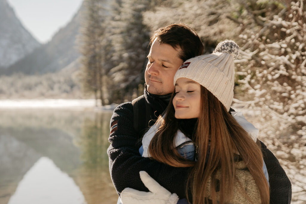 Couple embraces by snowy mountain lake.