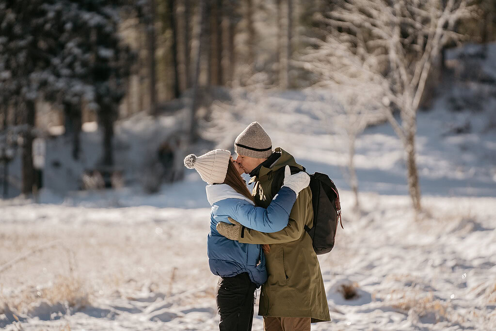 Couple kissing in snowy forest landscape.