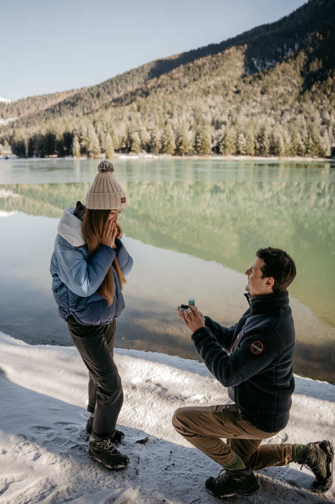 Man proposing to woman by snowy lake.