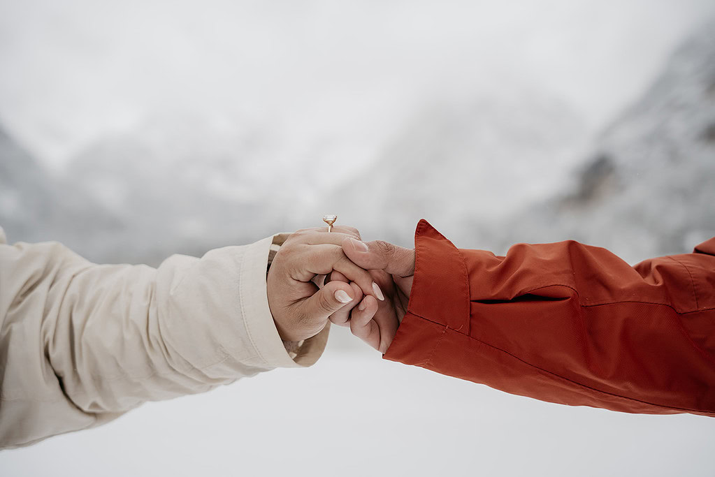 Couple holding hands with engagement ring visible.