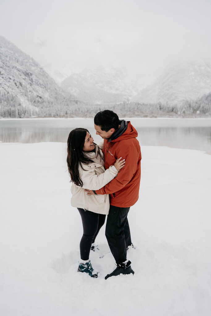 Couple embracing in snowy landscape by lake.