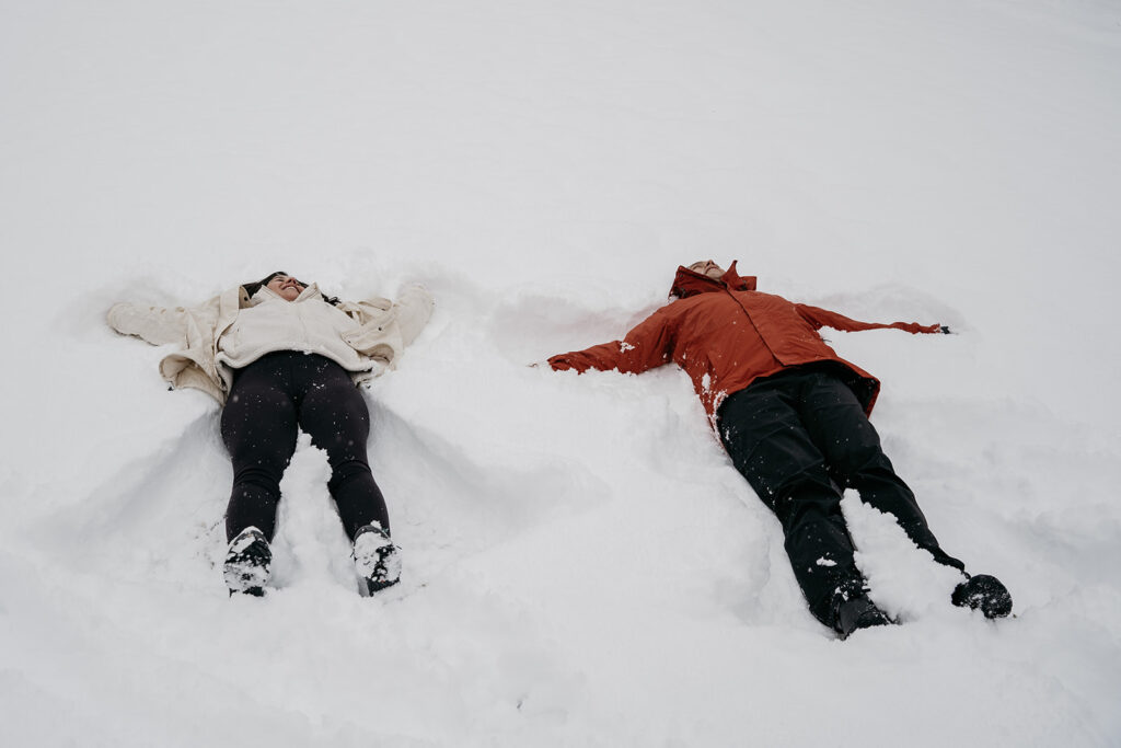 Two people making snow angels on snowy ground.