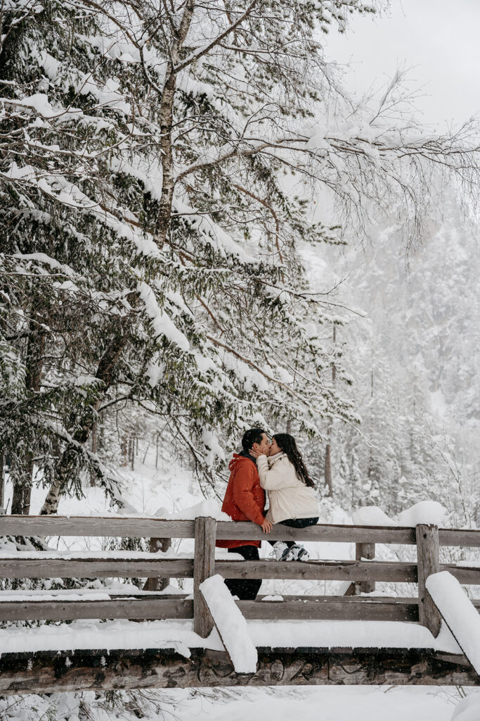 Couple kissing on a snowy bridge.