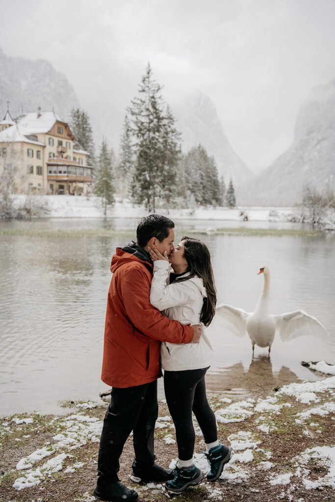 Couple kissing by snowy lake with swan.