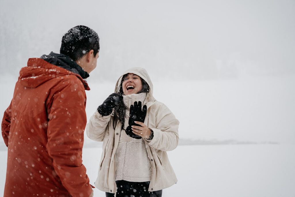 Couple laughing in snowy winter landscape.