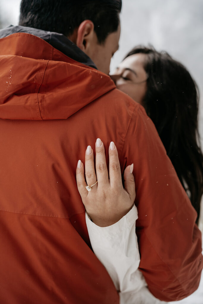 Couple embracing, showcasing engagement ring on hand.