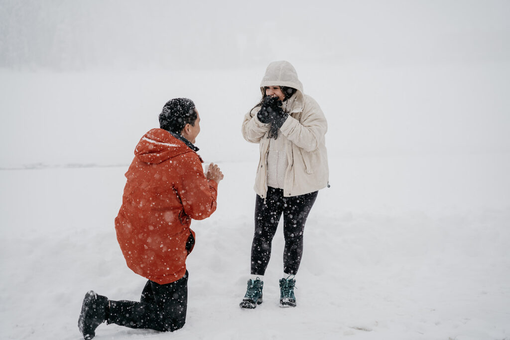 Couple engaged in snowy outdoor proposal scene.