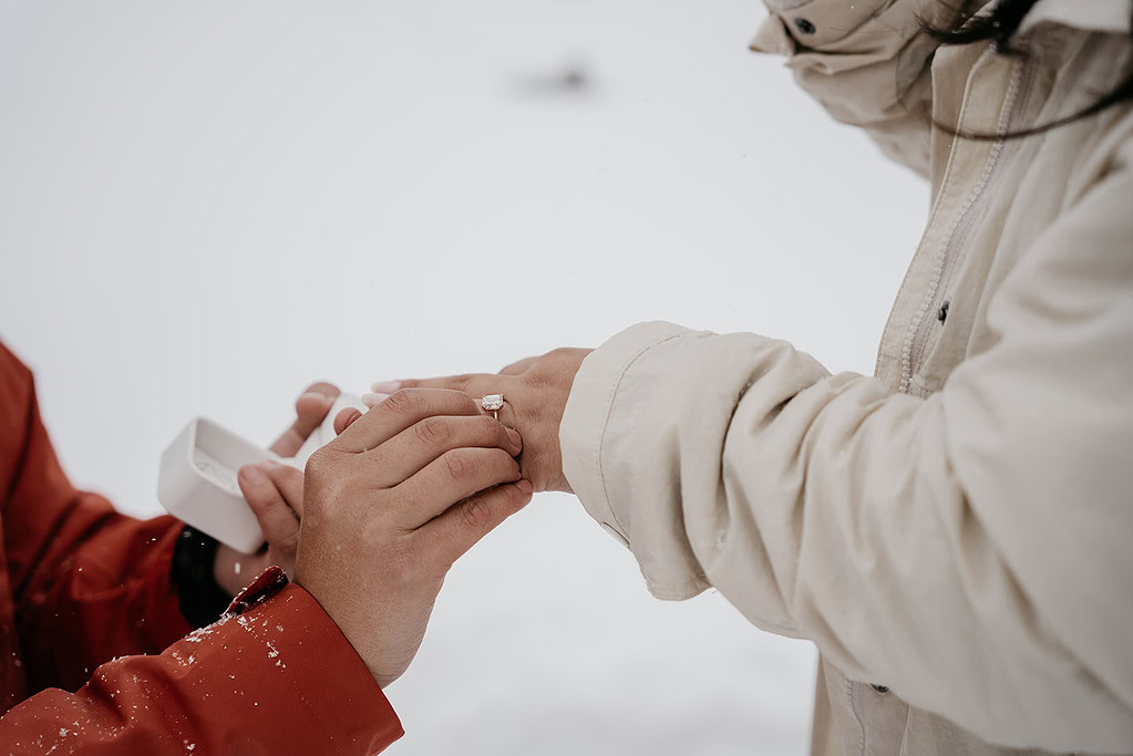 Person proposing with ring in snowy setting.