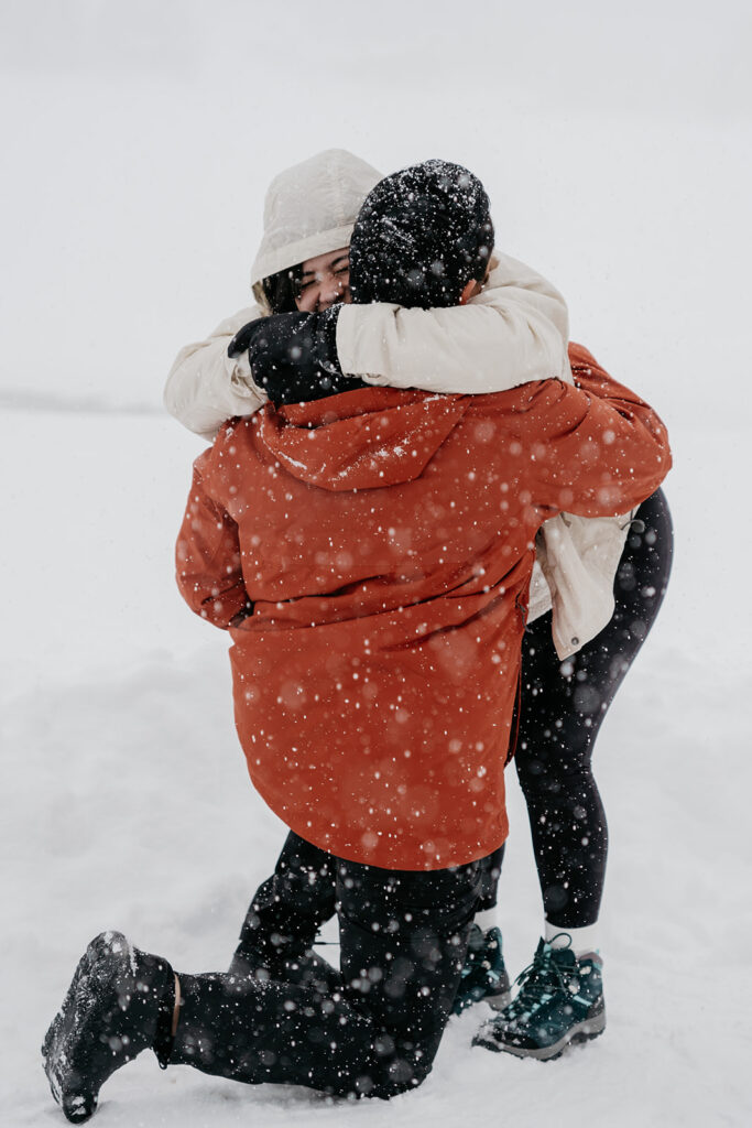 Couple hugging in snowy outdoor proposal scene.