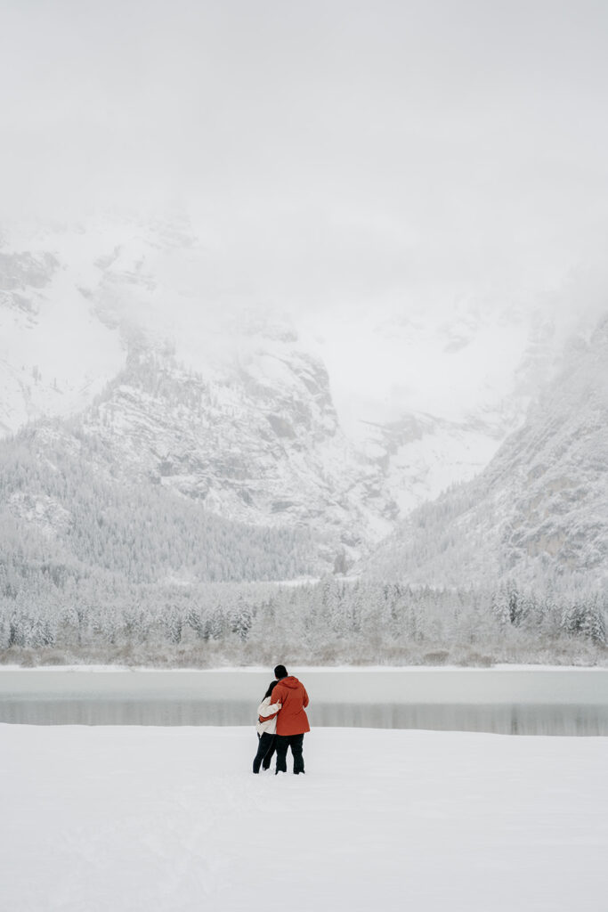 Couple embraces in snowy mountain landscape by lake.