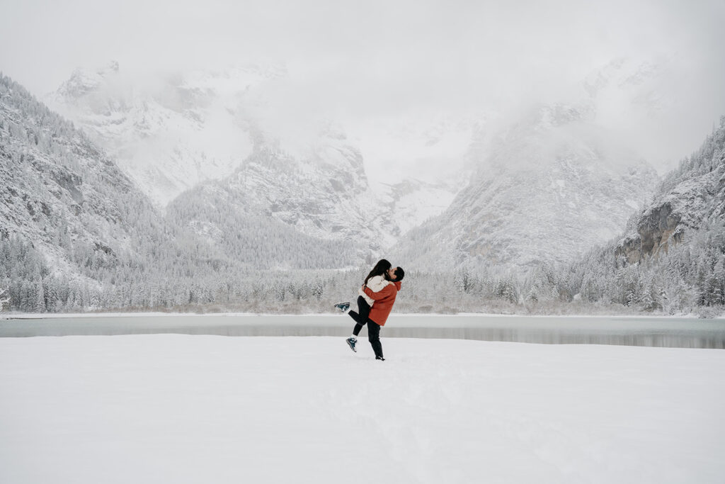 Couple embracing in snow with mountain backdrop.