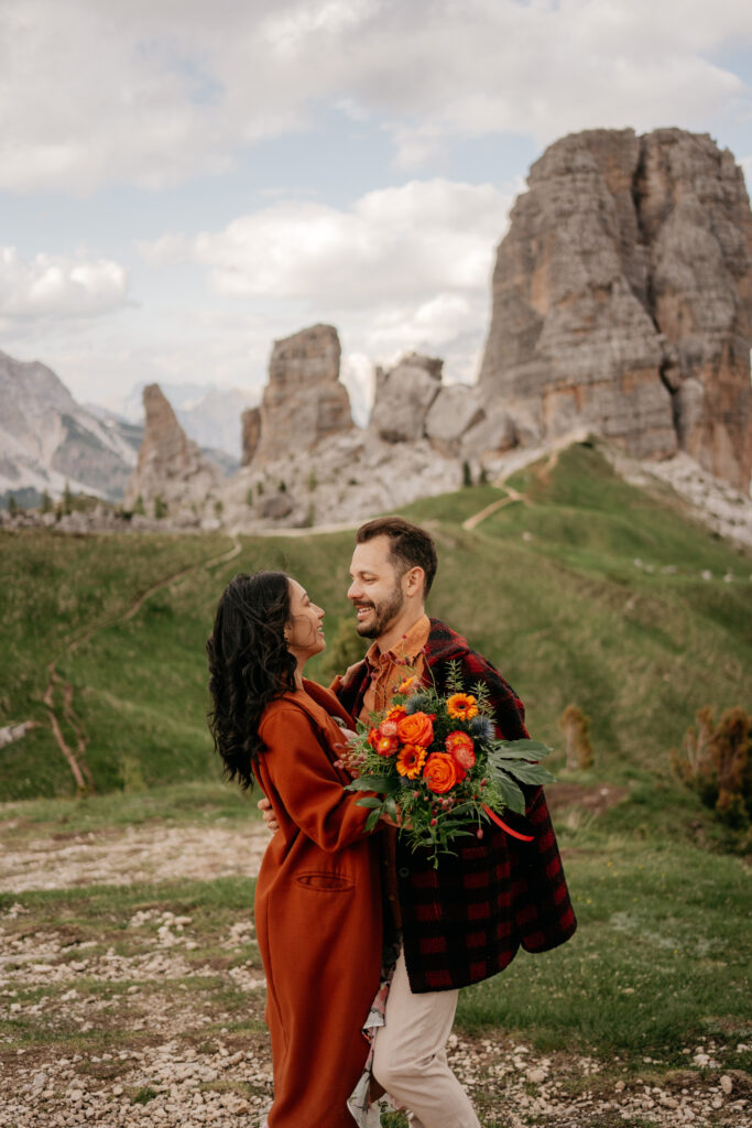 Couple embracing with bouquet in scenic mountain backdrop.