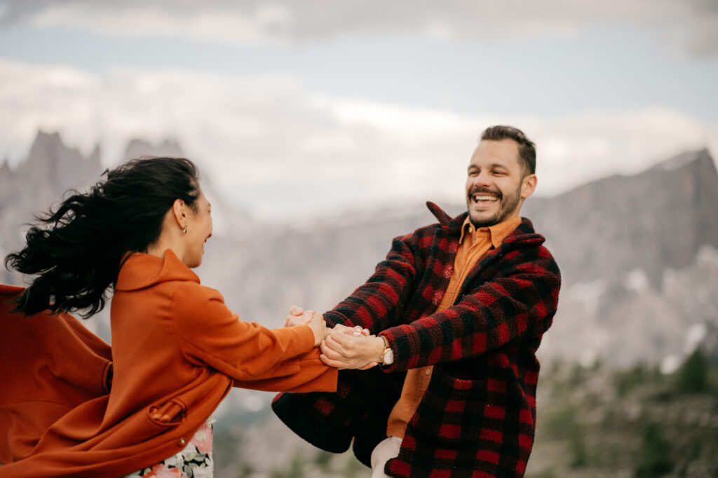 Couple laughing outdoors, holding hands, mountain background.