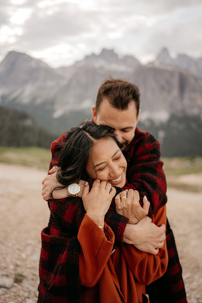 Couple hugging outdoors with mountain backdrop.