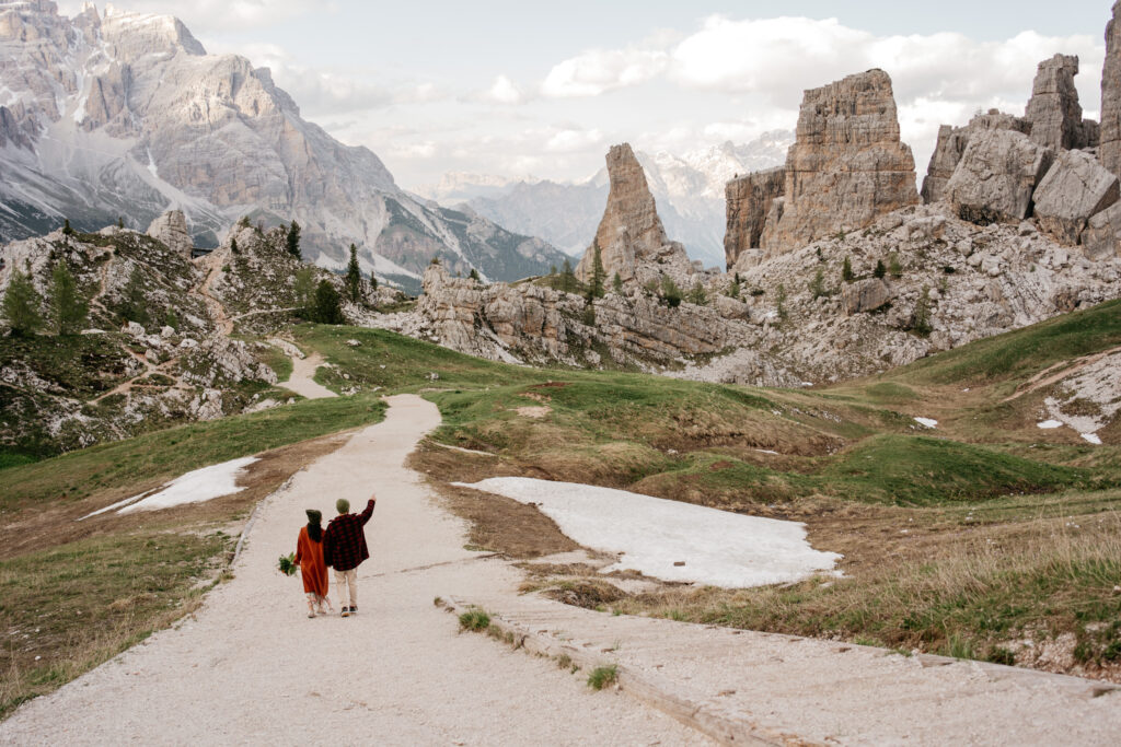 Couple walking on mountain trail with rocky landscape.