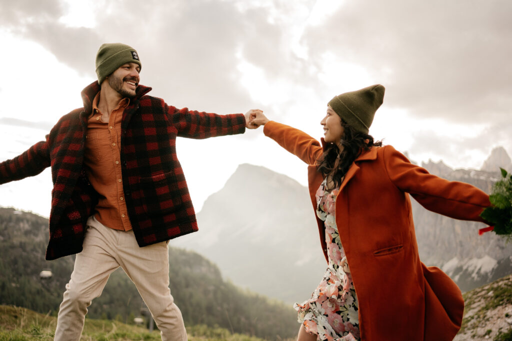 Couple smiling and holding hands outdoors in mountains.