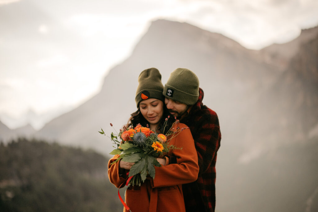 Couple embracing with flowers in mountainous landscape.