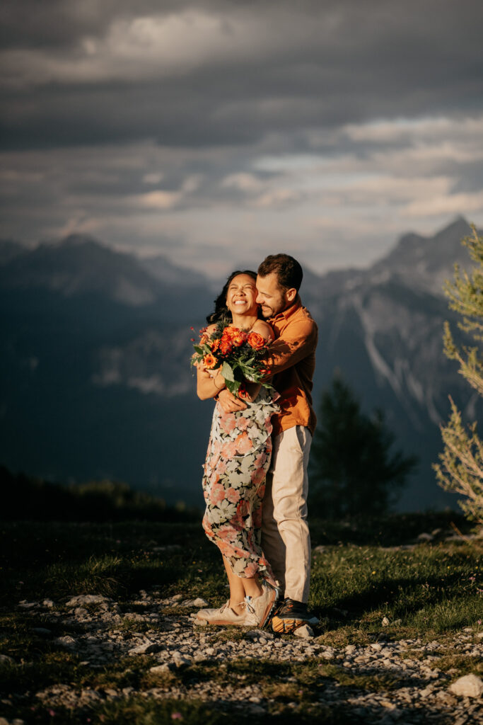 Couple embracing with mountain view, bright floral dress.