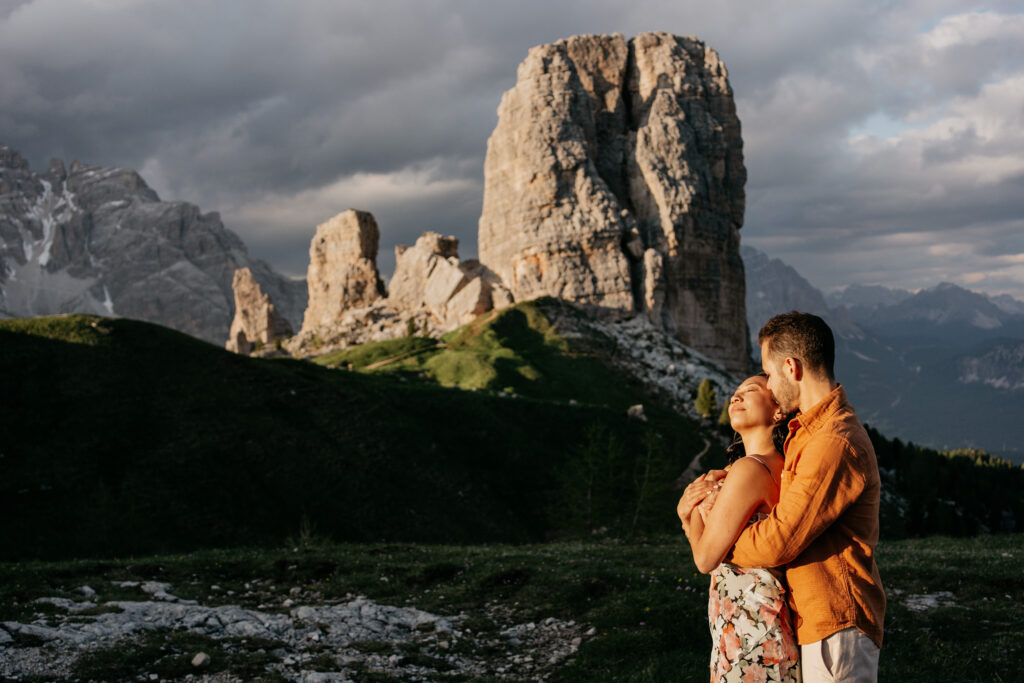 Couple embraces against mountainous landscape backdrop.